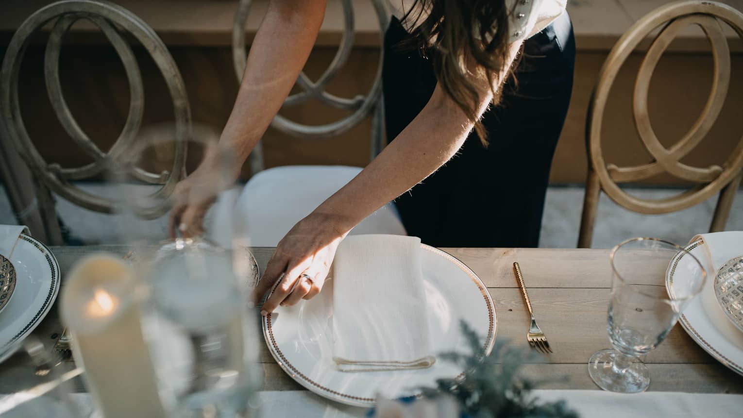 Person putting place settings at a table with candles.