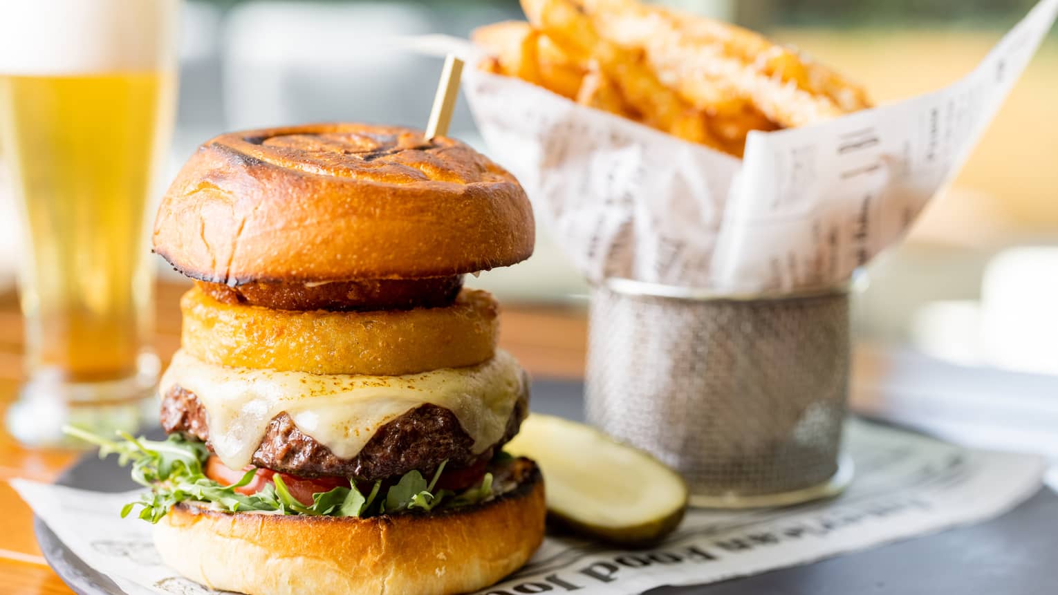 A burger next to a pickle and fries on a black plate.