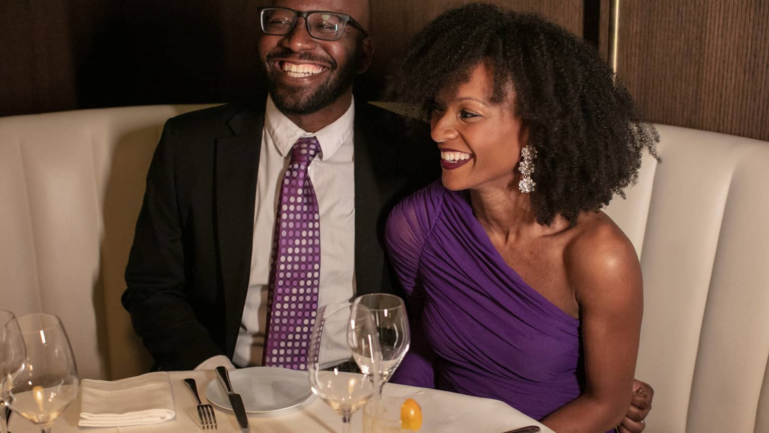 A man and woman in nice clothing sitting at a dining booth.