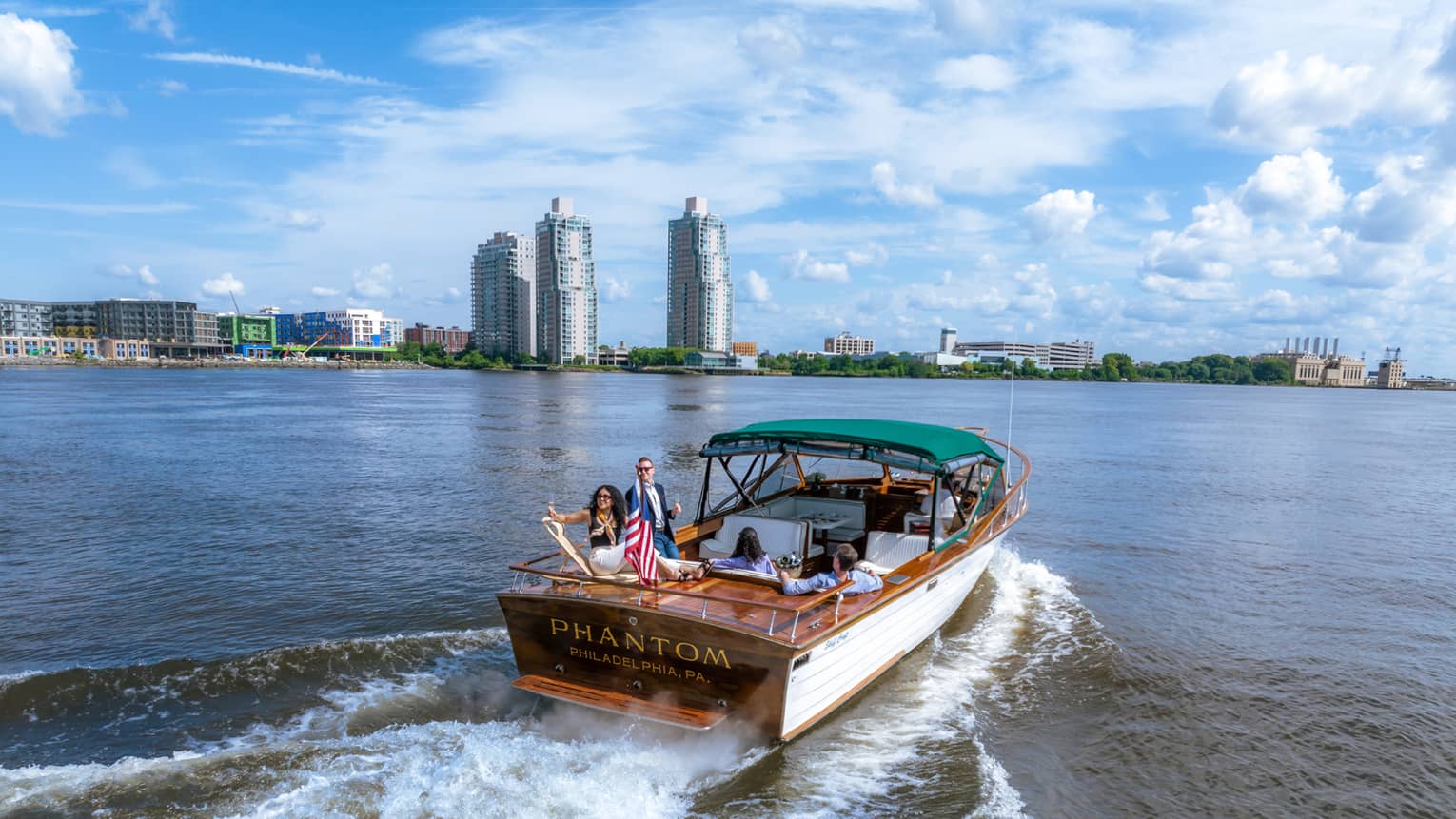 Guests on a boat in the water with city buildings in the background.
