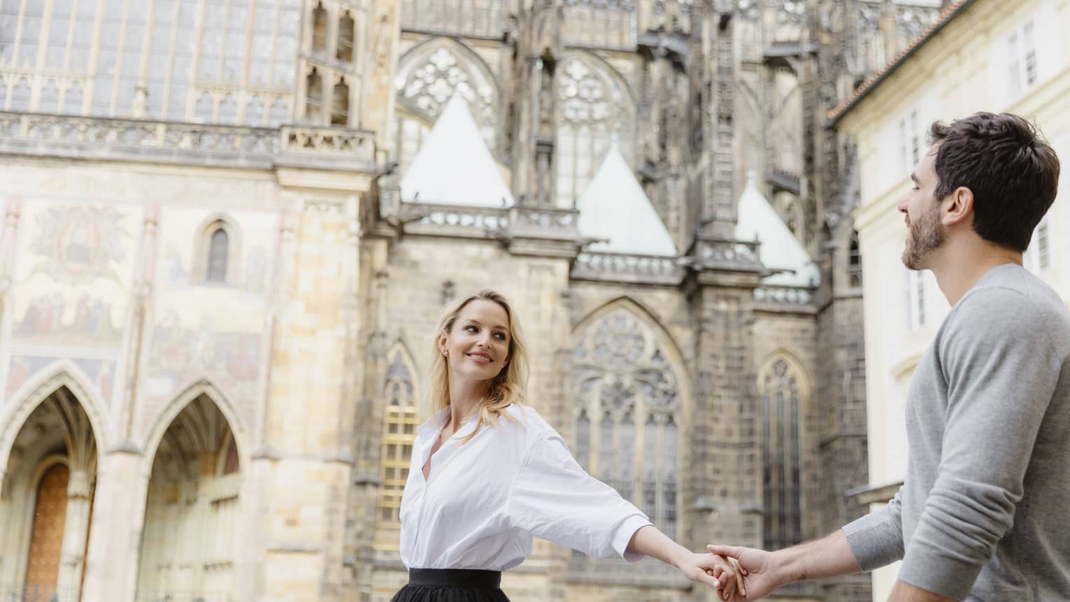 Couple smiling, holding hands with arms stretched as they tour historic city