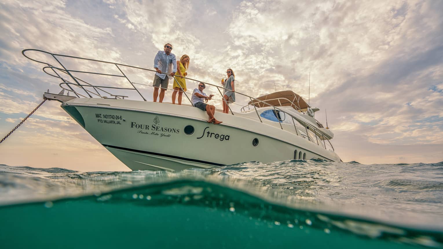 White Four Seasons motor yacht anchored in ocean, two men and two women look out at sea
