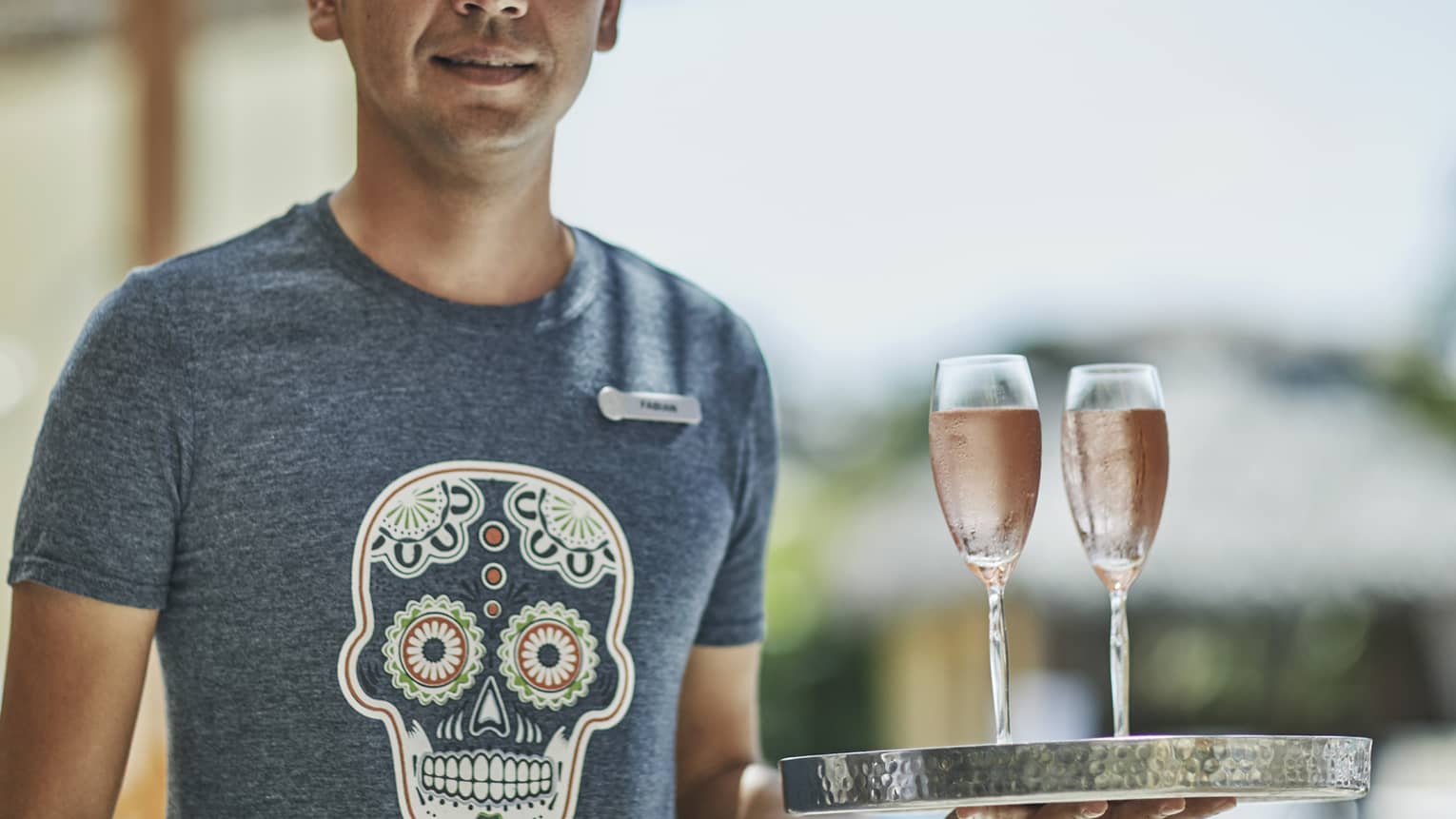 A staff member holding a tray with two glasses of sparkling wine on top.