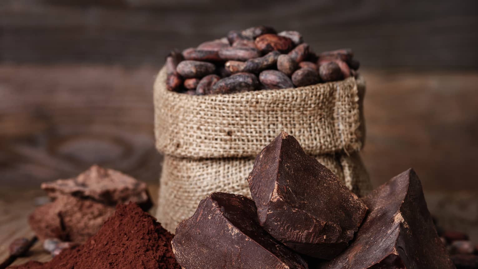 Chunks of chocolate, cocoa powder and coffee beans in a burlap sack