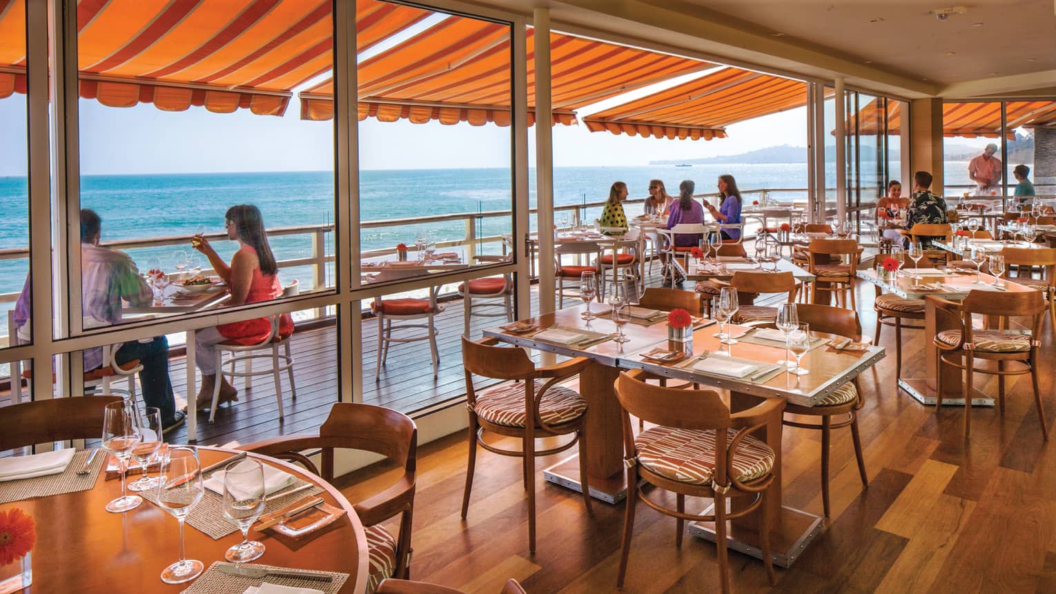 Dining tables chairs on hardwood floors, sliding glass wall to diners under orange awning
