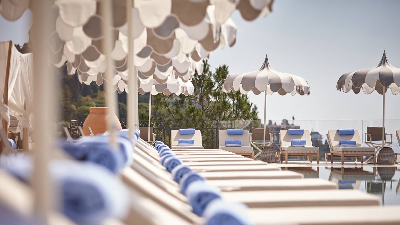 A row of lounge chairs with umbrellas and towels along the side and end of a pool