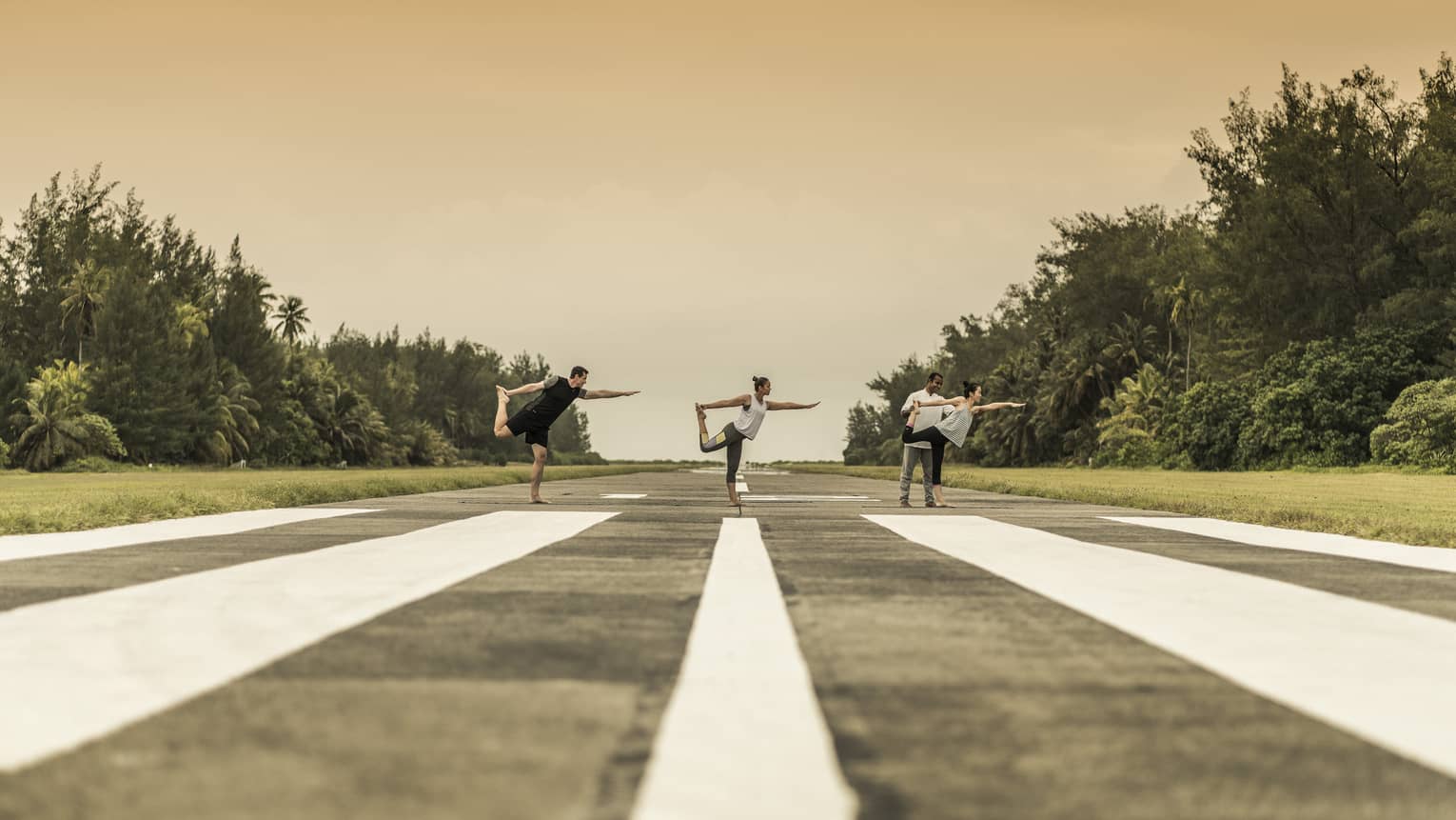 Three people perform dancers pose with instructor on runway surrounded by trees 