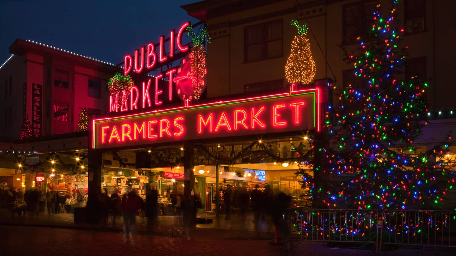 Sign that says "Farmers Market" with a Christmas tree with lights beside it.