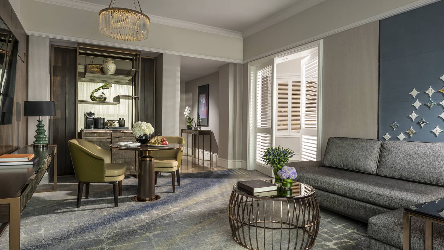 Gold dining chairs around small dining table by brass wire table, L-shaped grey sofa