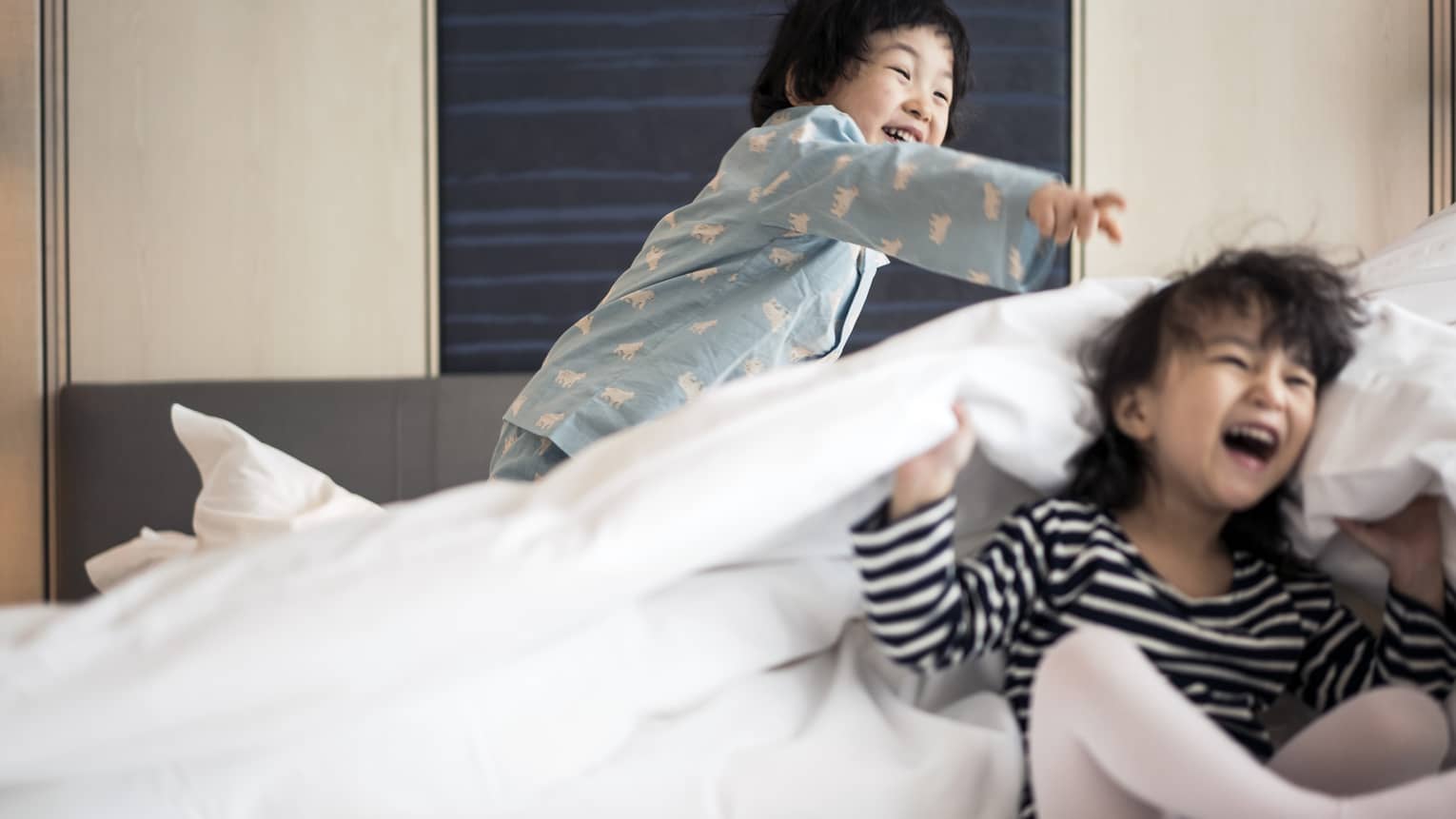 Two laughing children play among the bedsheets