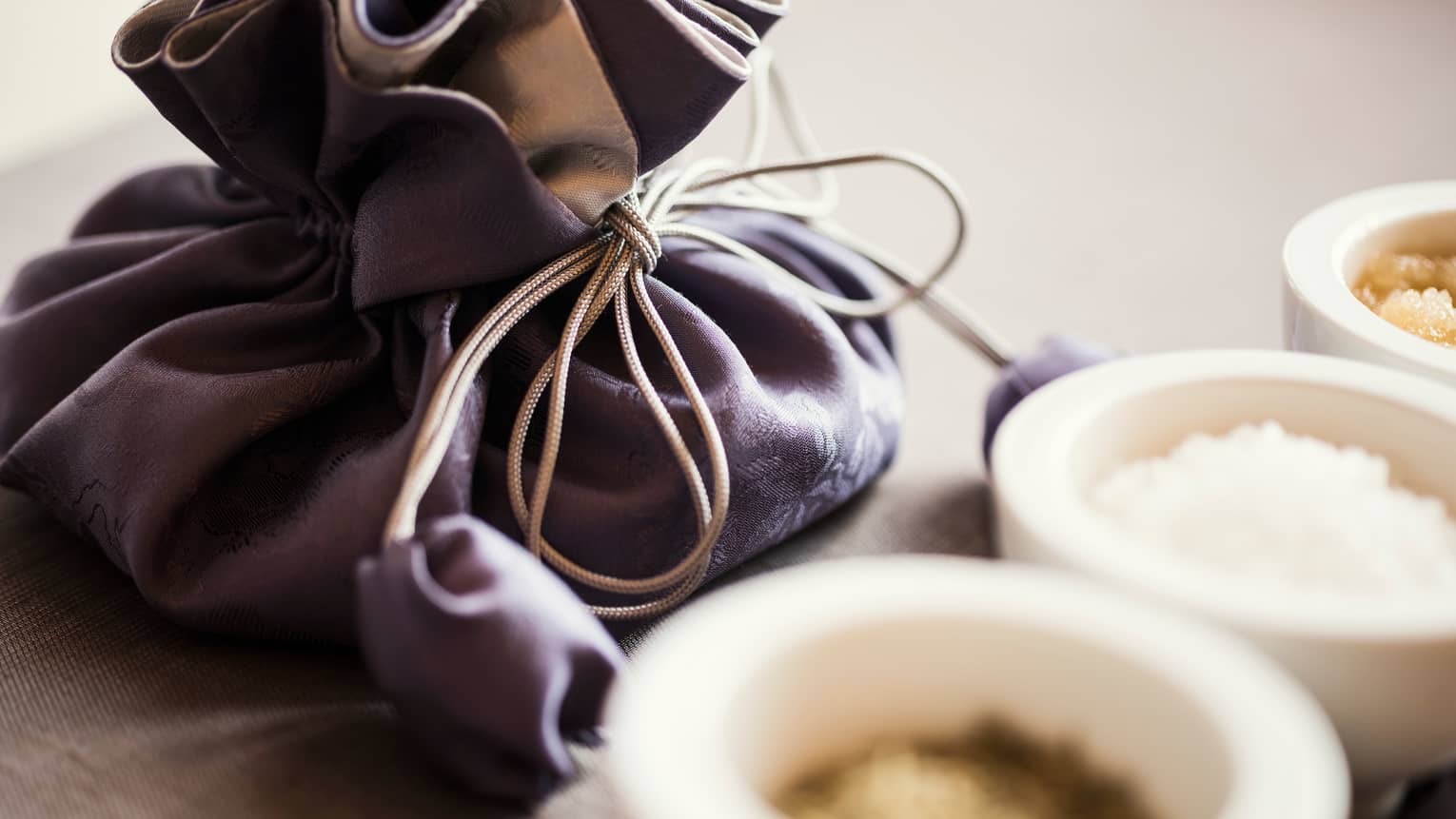 Dark silk pouch with tie behind small white ceramic bowls with spa salts