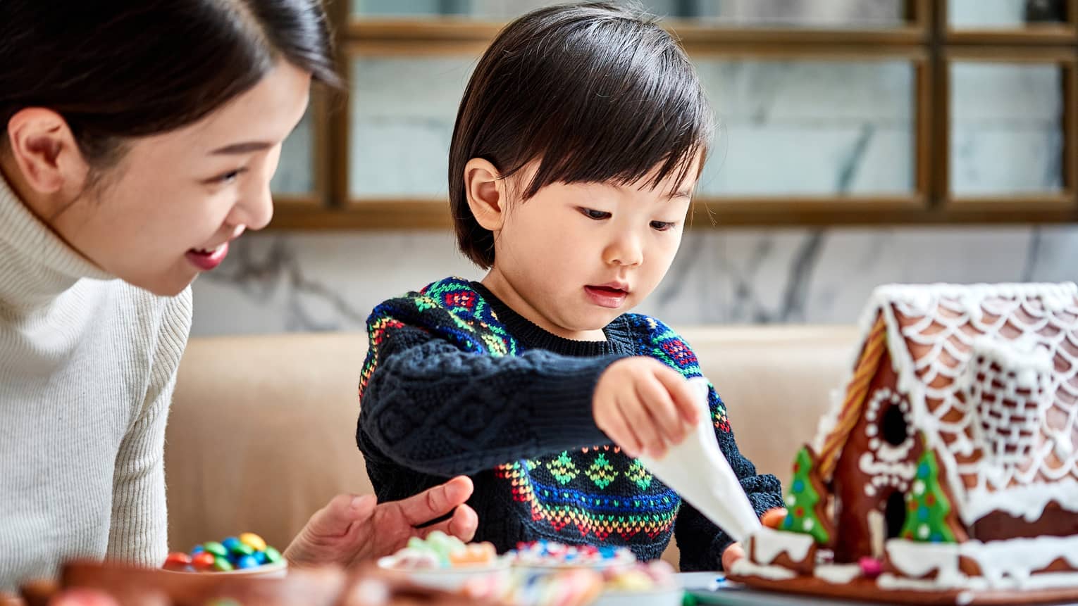 A mother and child make gingerbread houses together