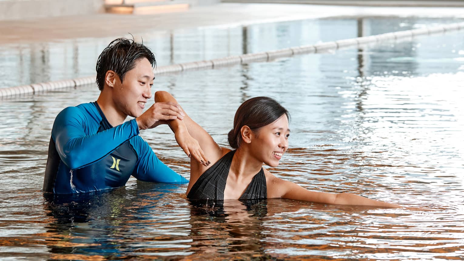 Swimming instructor helps woman position arm in indoor swimming pool