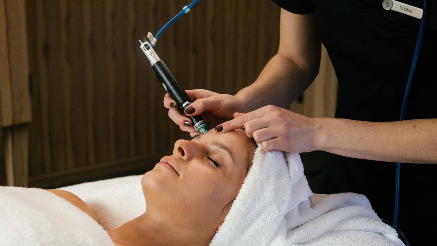 A guest laying on a spa table with a towel wrapped around their hair and getting a facial