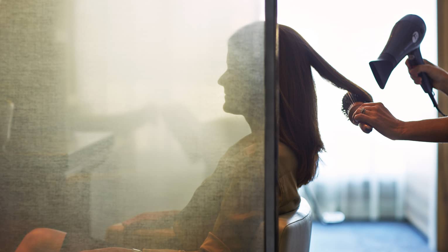 Silhouette of woman behind salon screen as hairdressers brushes, blow dries hair