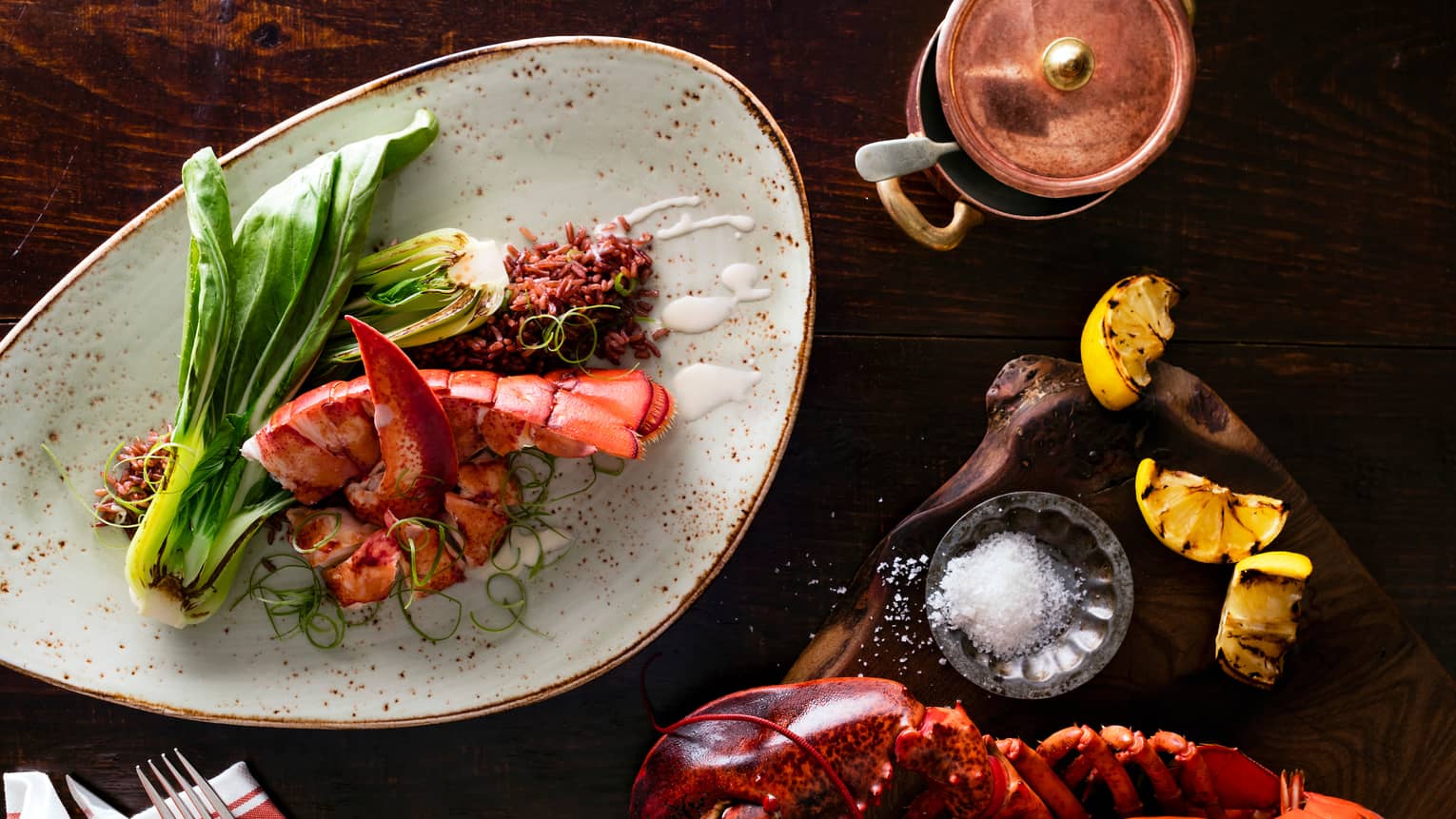 Aerial view of red lobsters, tails on plates with charred greens, black rice