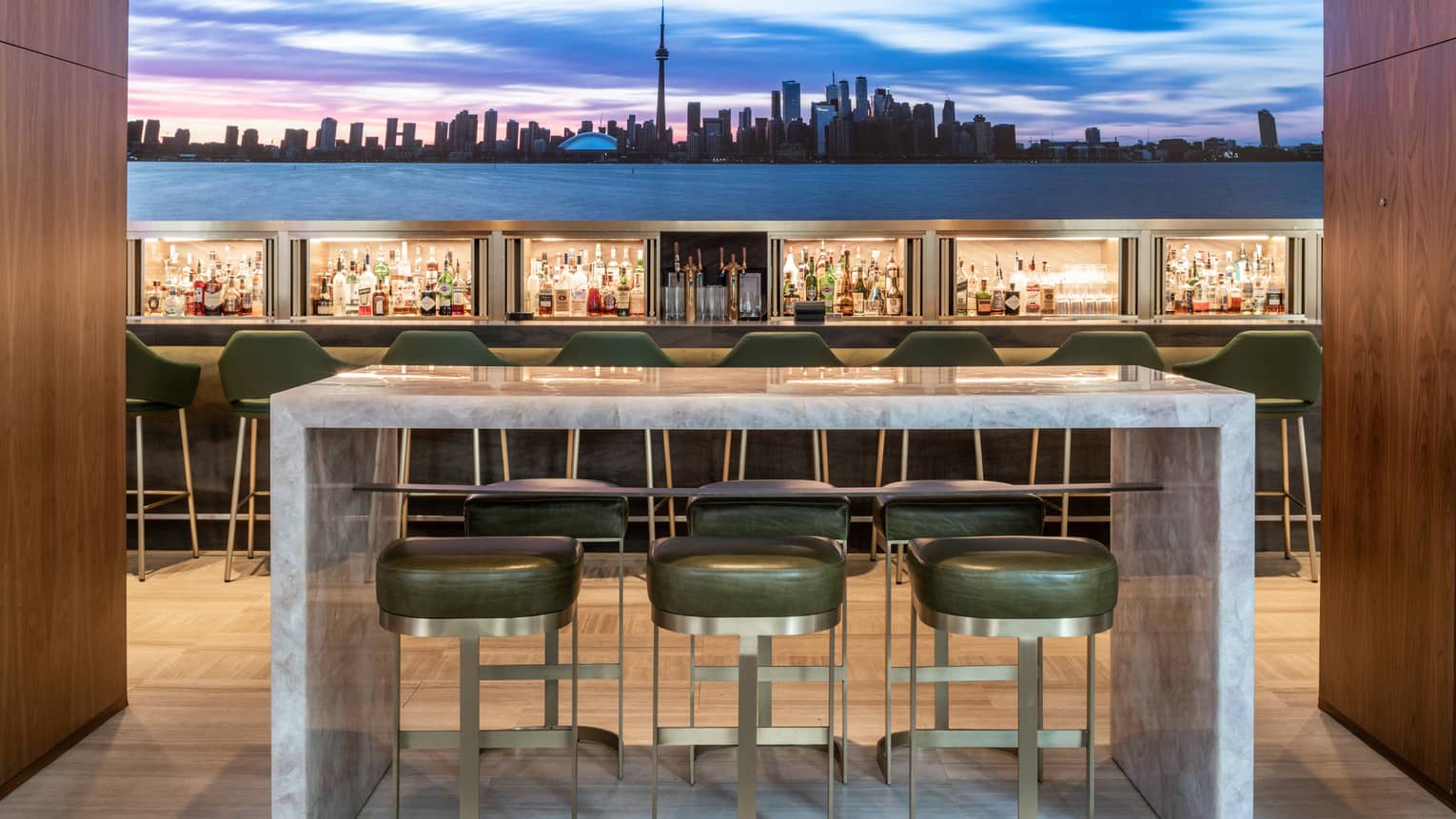 Upholstered high chairs at a marble table near the bar with an image of the skyline behind it