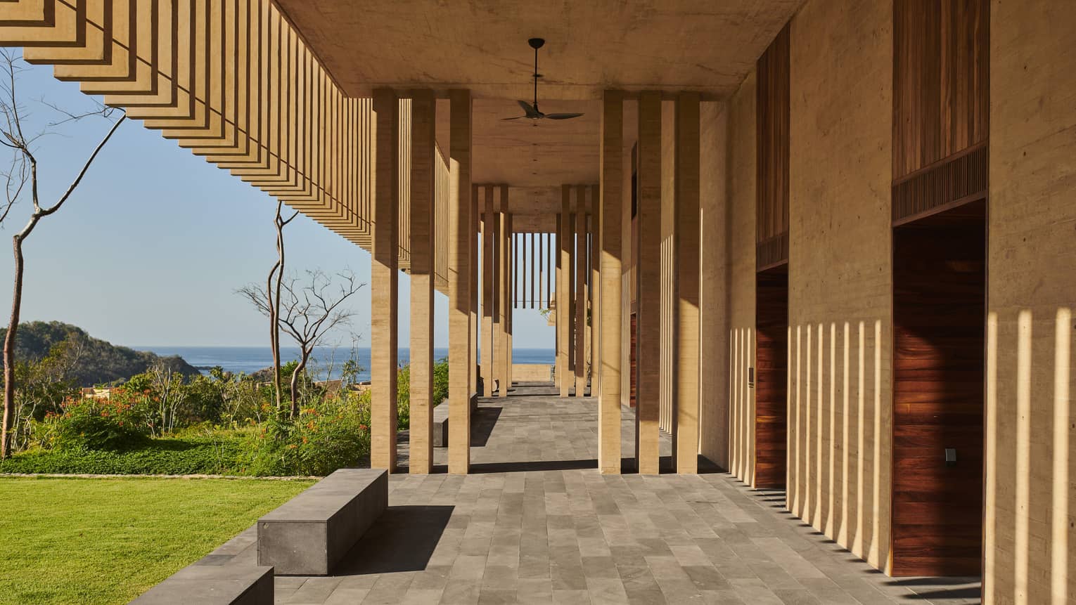 Walkway with columns and gray bricks, with a view of the ocean.