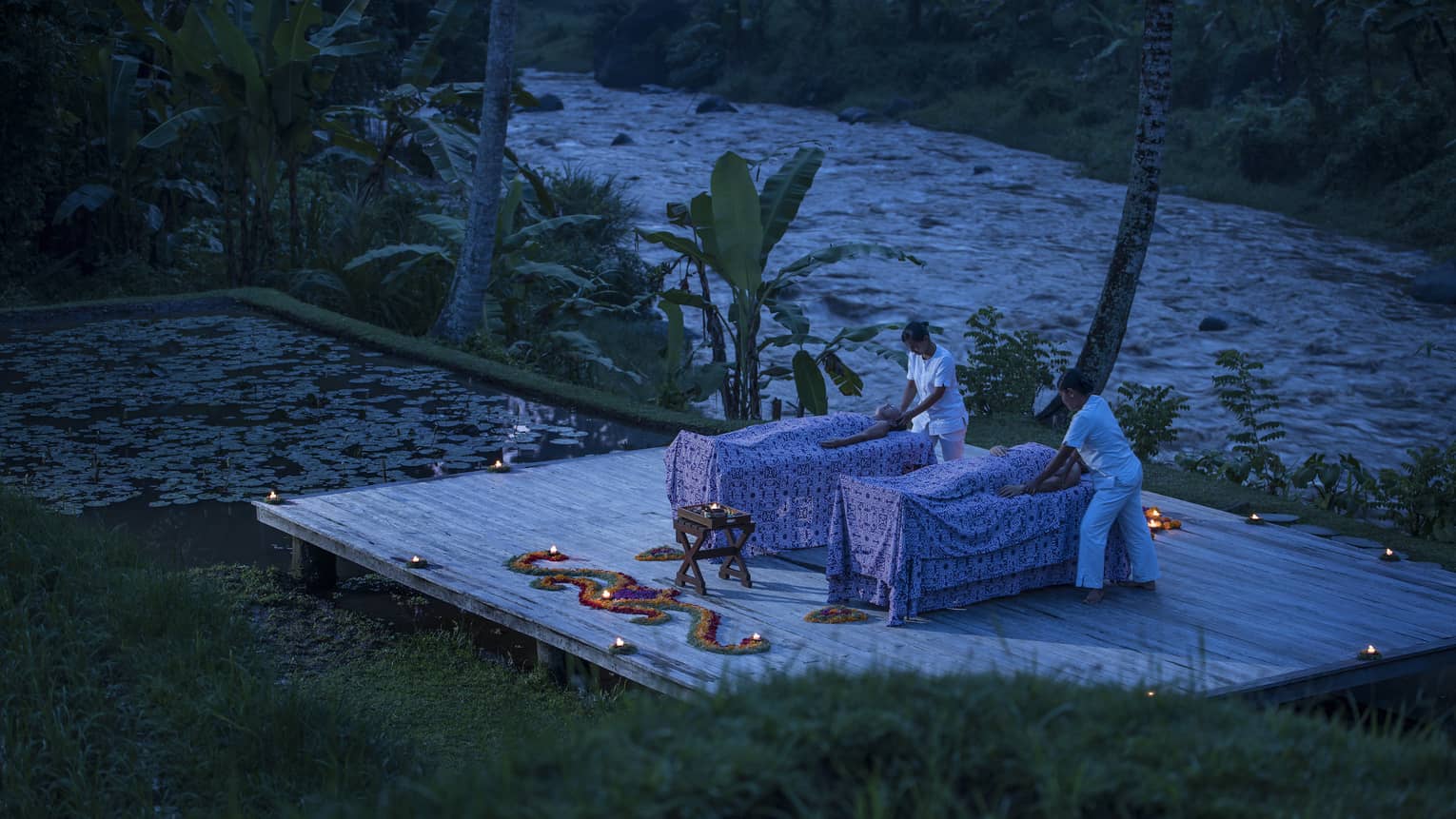 Two guests receive candle-lit massages on a dock at night 