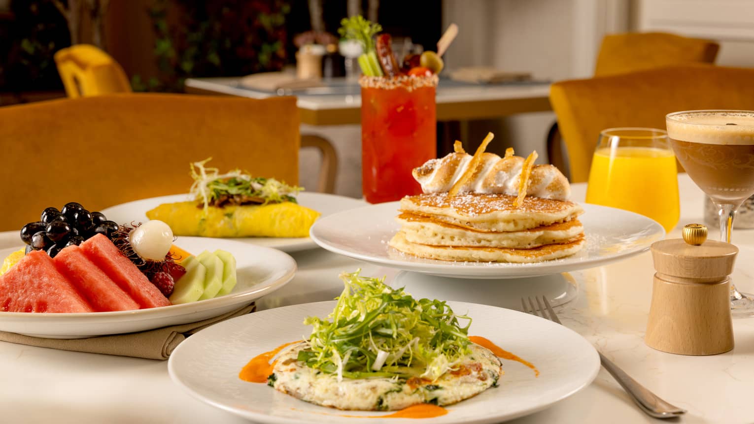 A variety of brunch dishes and drinks displayed on a white table, including pancakes and fruit.