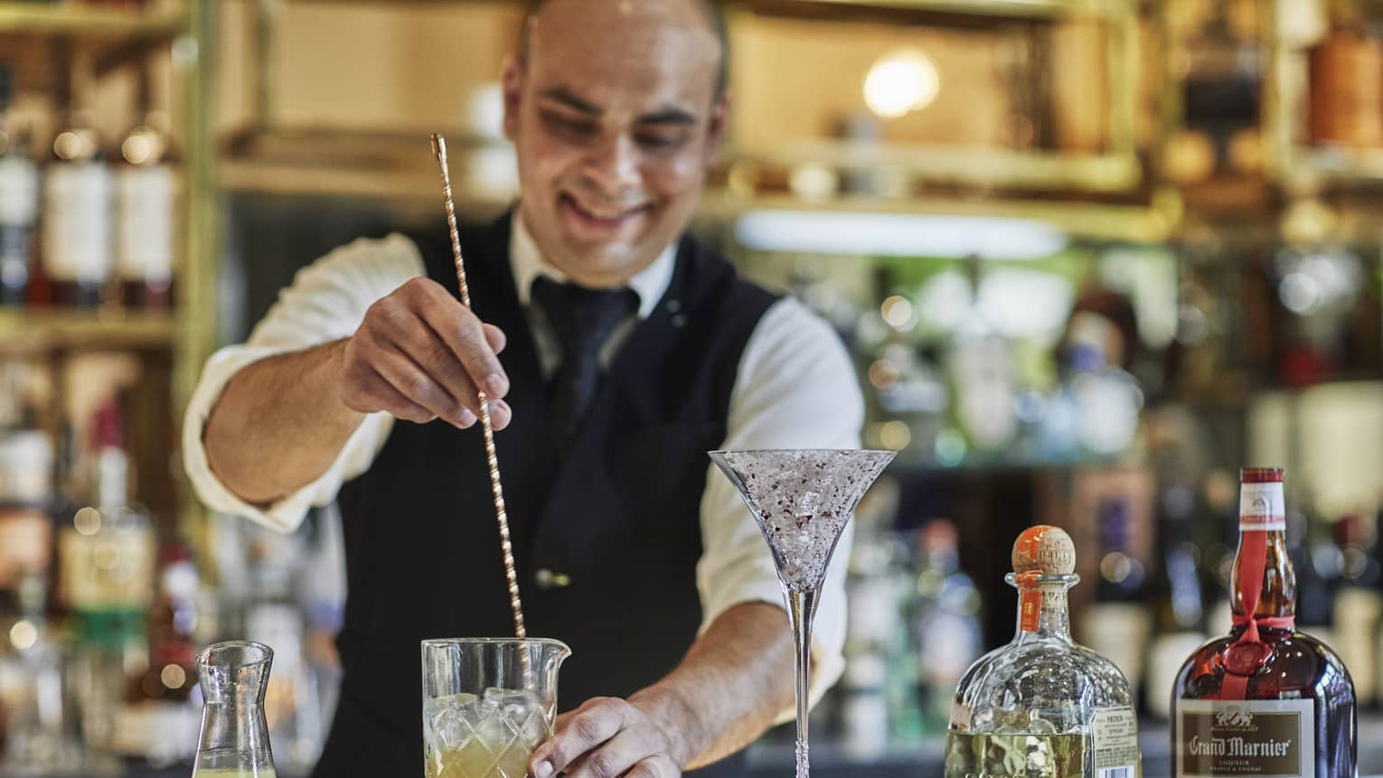 Bartender stirs cocktail with large swizzle stick on bar 