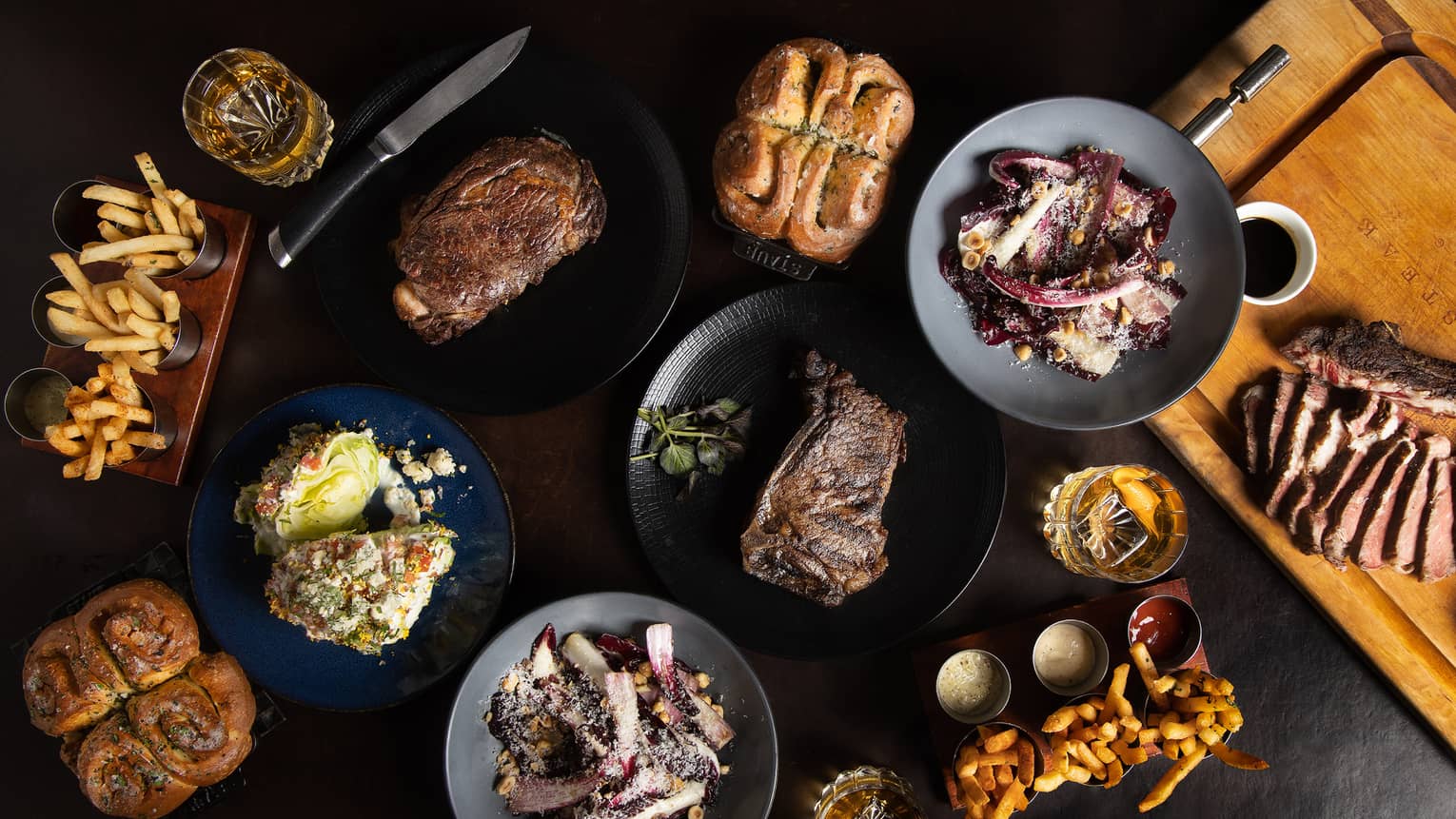 Multiple plates of food, including french fries, steak and bread rolls.