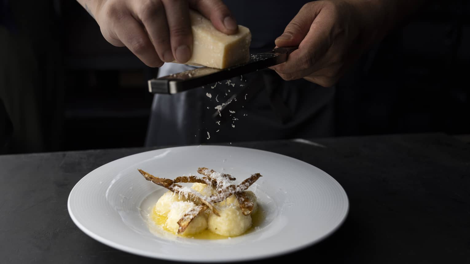 Person grating cheese over a bowl of food.
