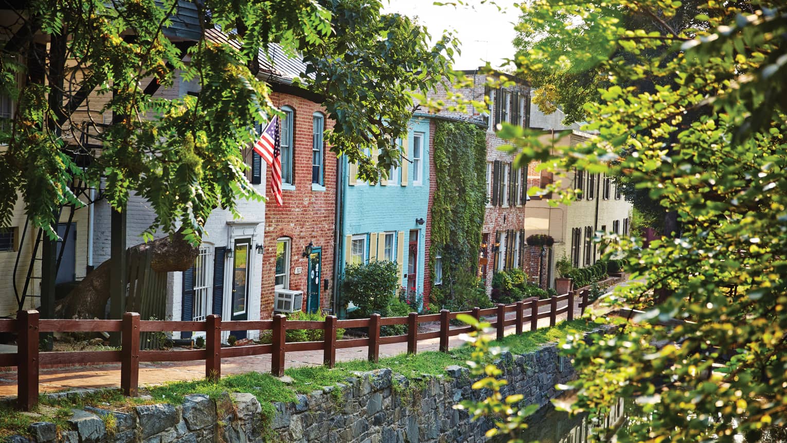 Row of colorful houses in city, road and wooden fence along a canal with trees