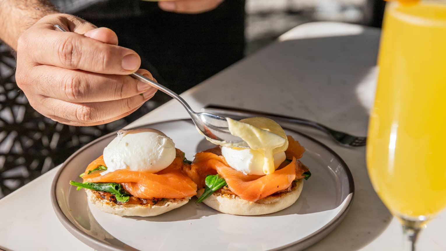 A person eating Eggs Benedict with silverware on the side