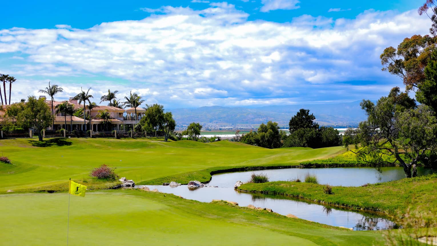 A golf course with a putting green, lake and palm trees