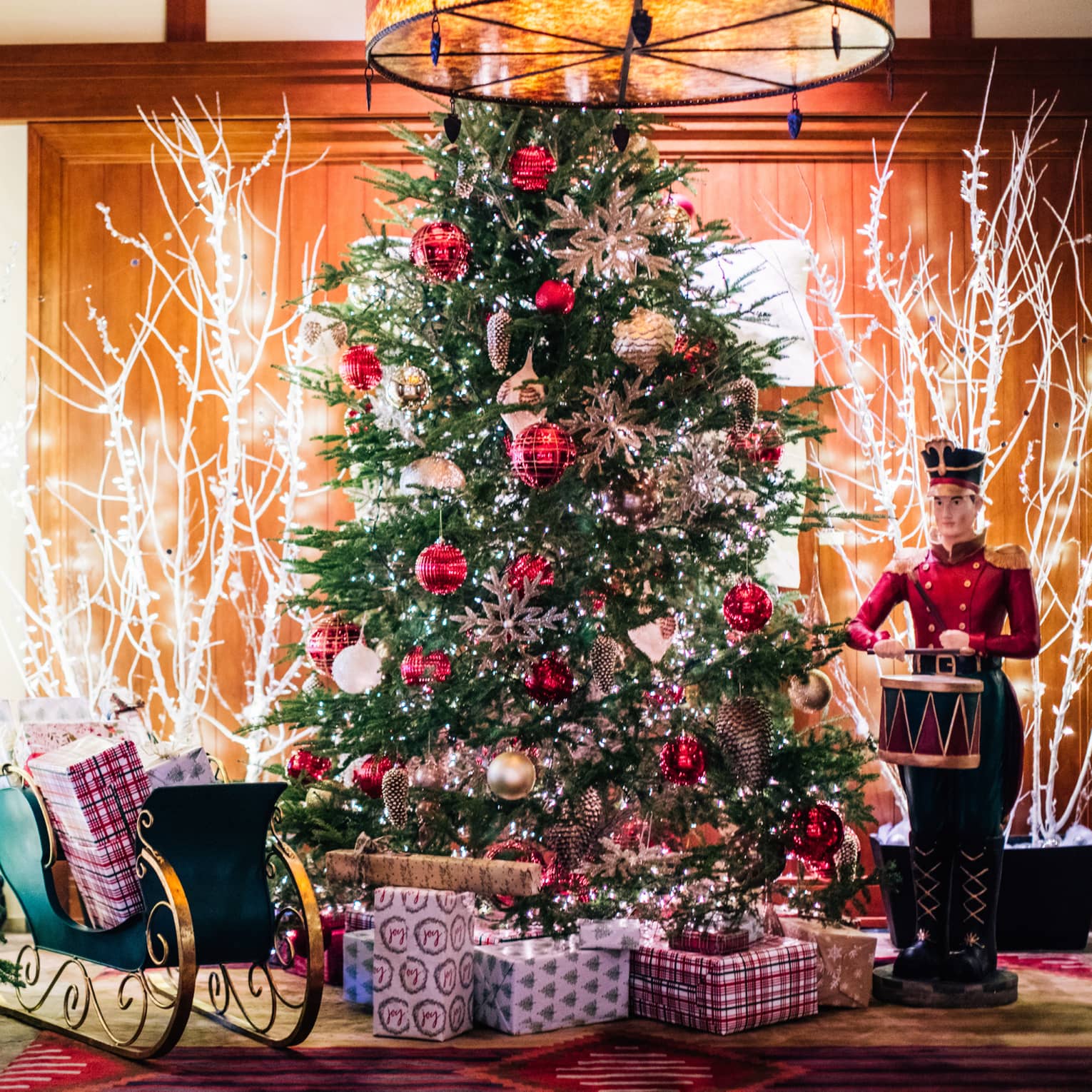 A Christmas tree with a toy soldier and presents around it.