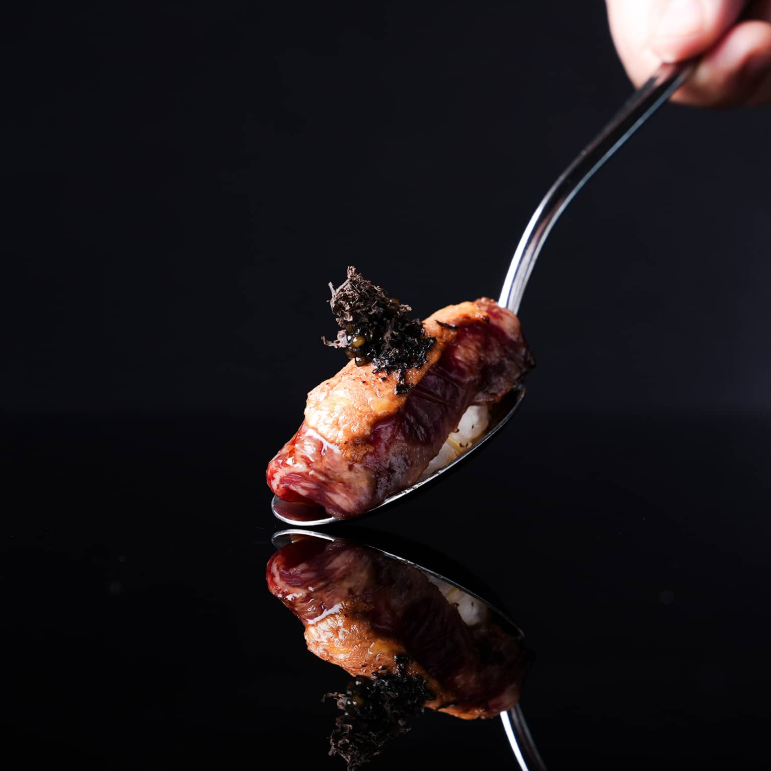 Spoon holding a piece of nigiri sushi on a black backdrop