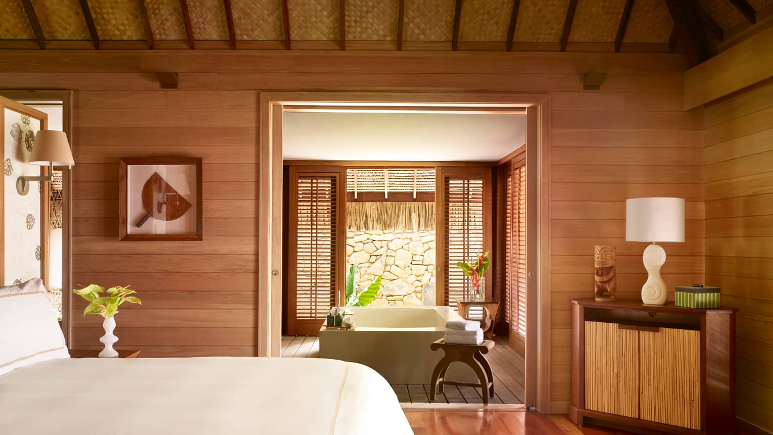 Fenua beachfront villa bedroom with white bed, wood decor, looking into room with square spa tub, patio door