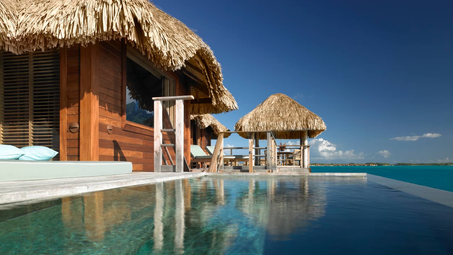 View from plunge pool of water suite bungalow, looking up at patio chairs and thatched roofs