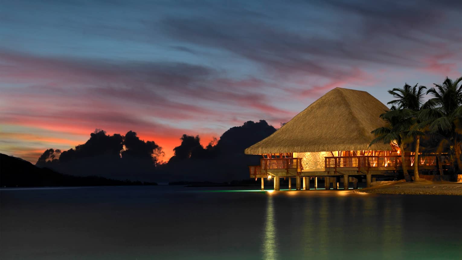 Exterior view of Sunset Restaurant and Bar with thatched roof and patio at sunset