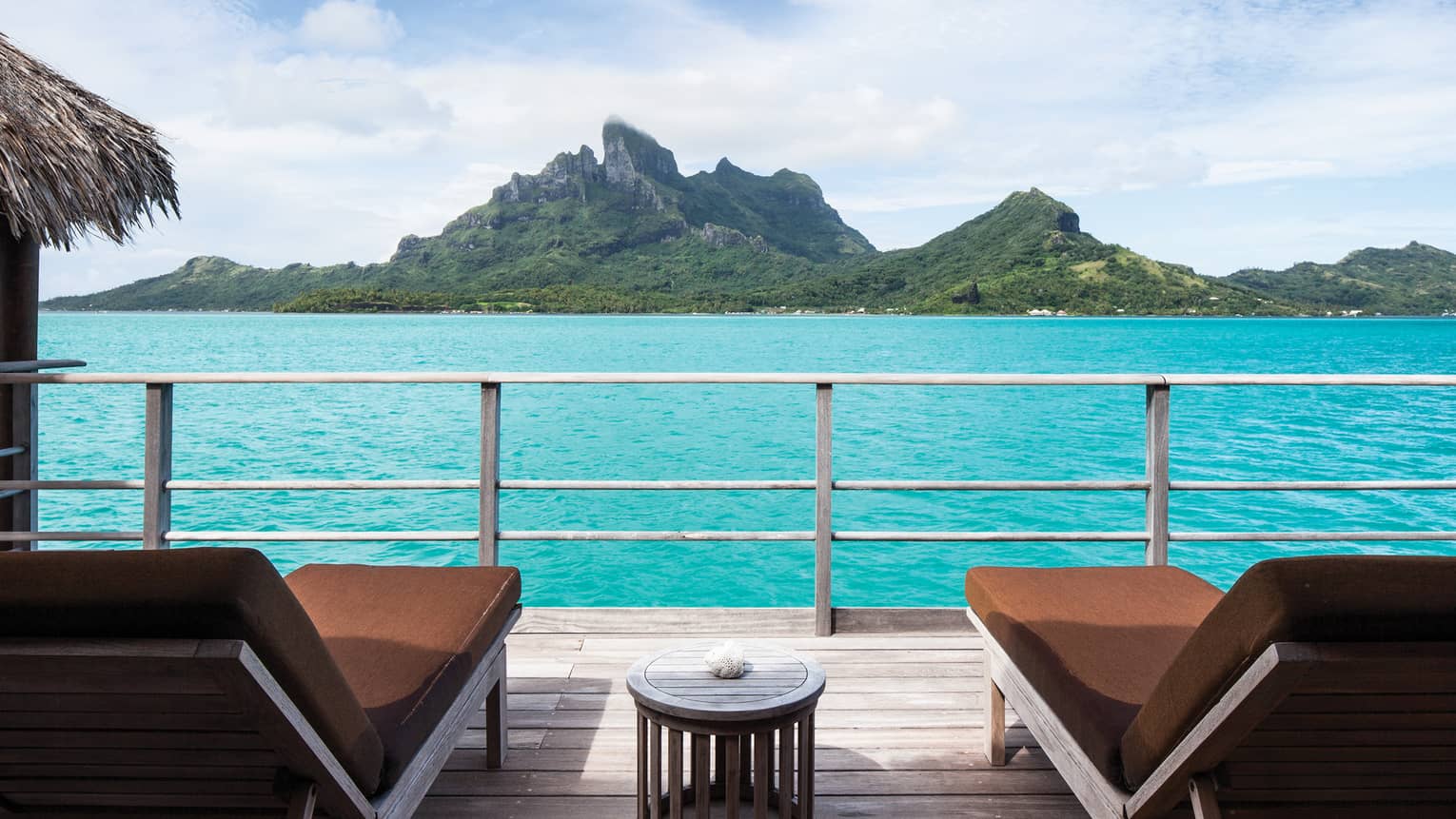 Two brown padded deck chairs looking out at blue lagoon with mountains in background