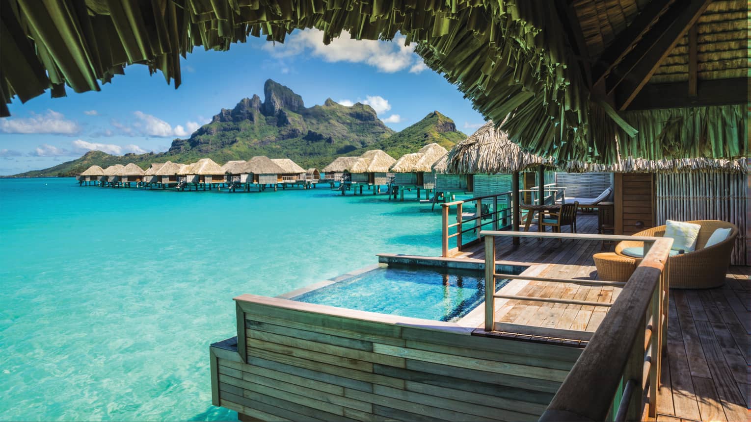 View from under thatched roof of Poerava Overwater Bungalow Suite with plunge pool over lagoon
