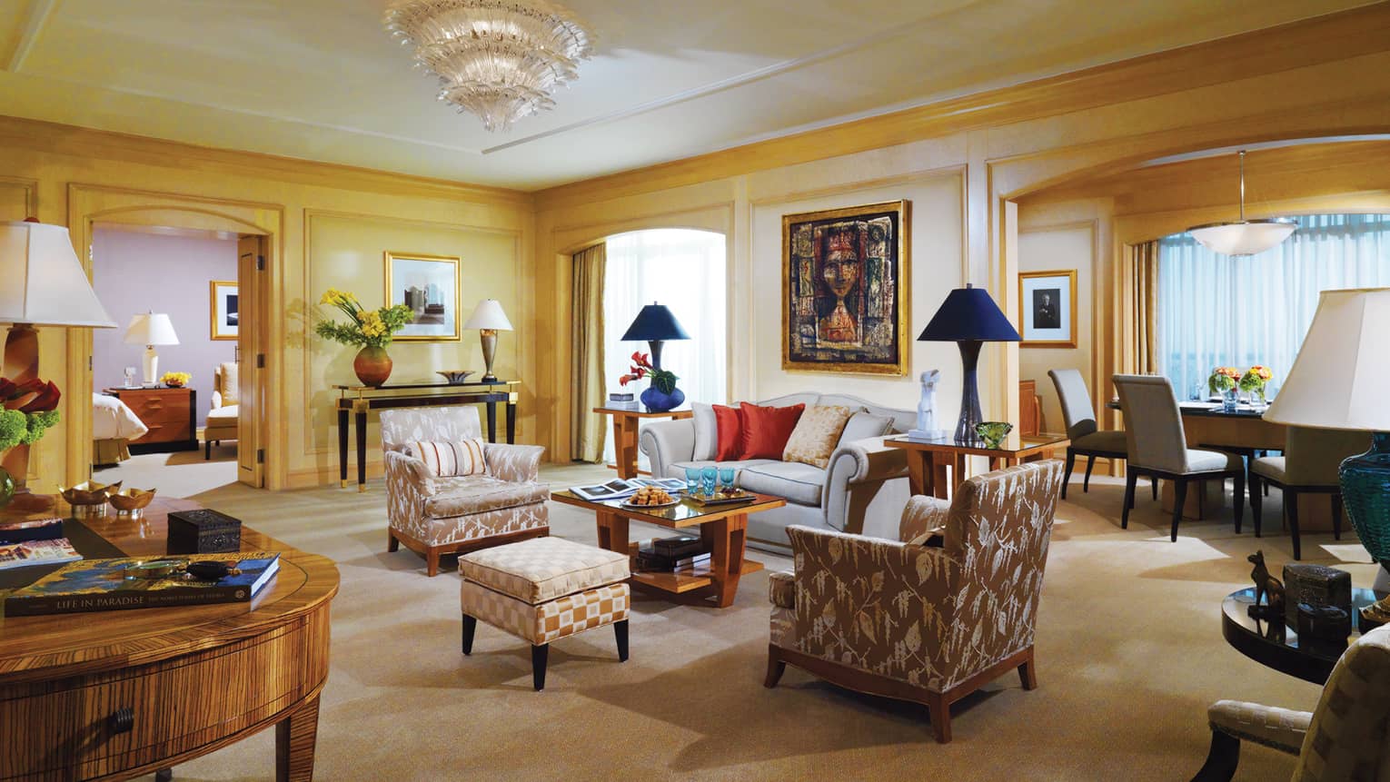 Large Presidential Suite living room with blue sofa, patterned chairs, crystal chandelier, adjoining dining and bedroom