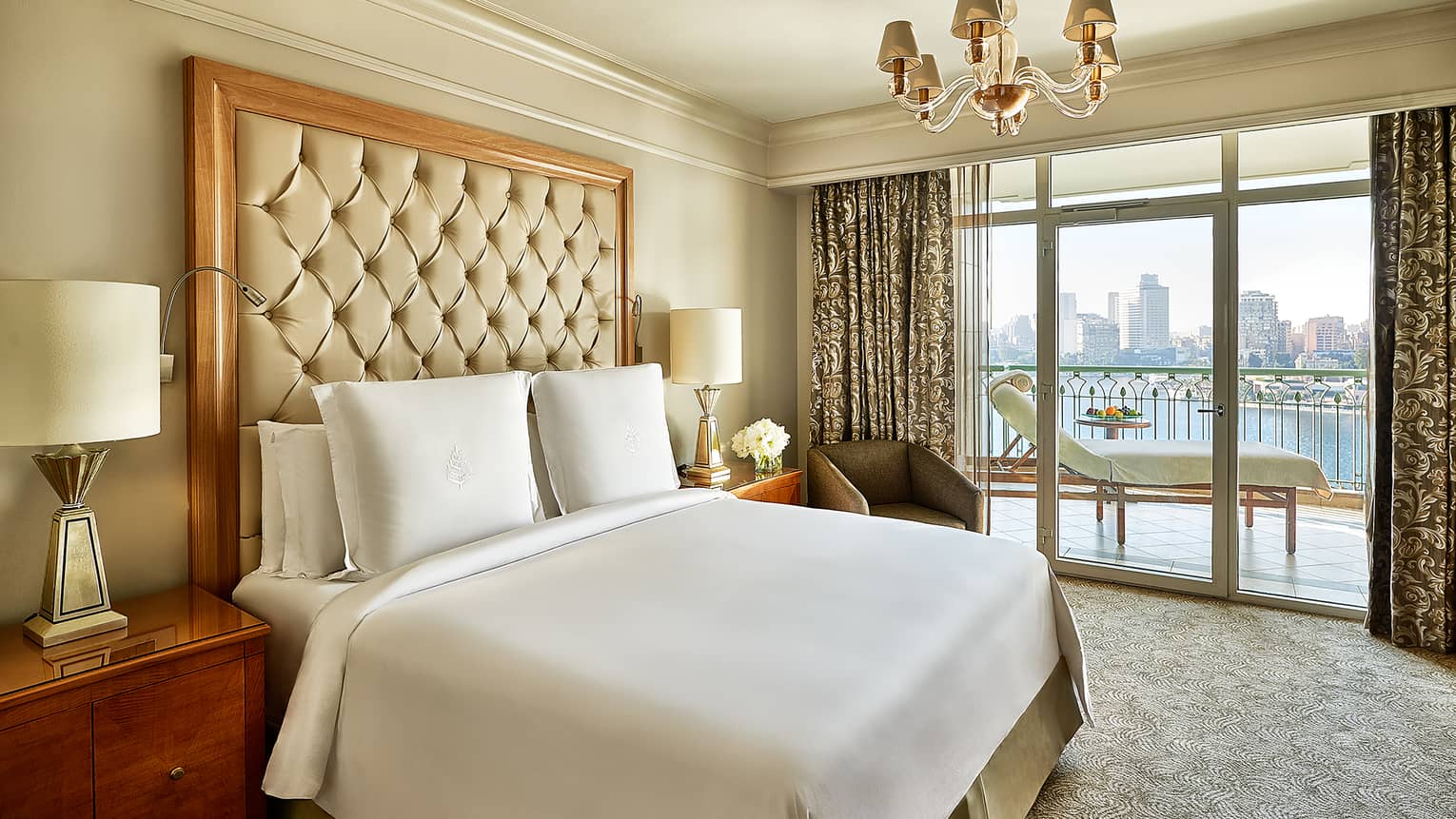 Executive Suite bed with white bedspread, pillows and padded headboard, door to balcony with white chaise lounge