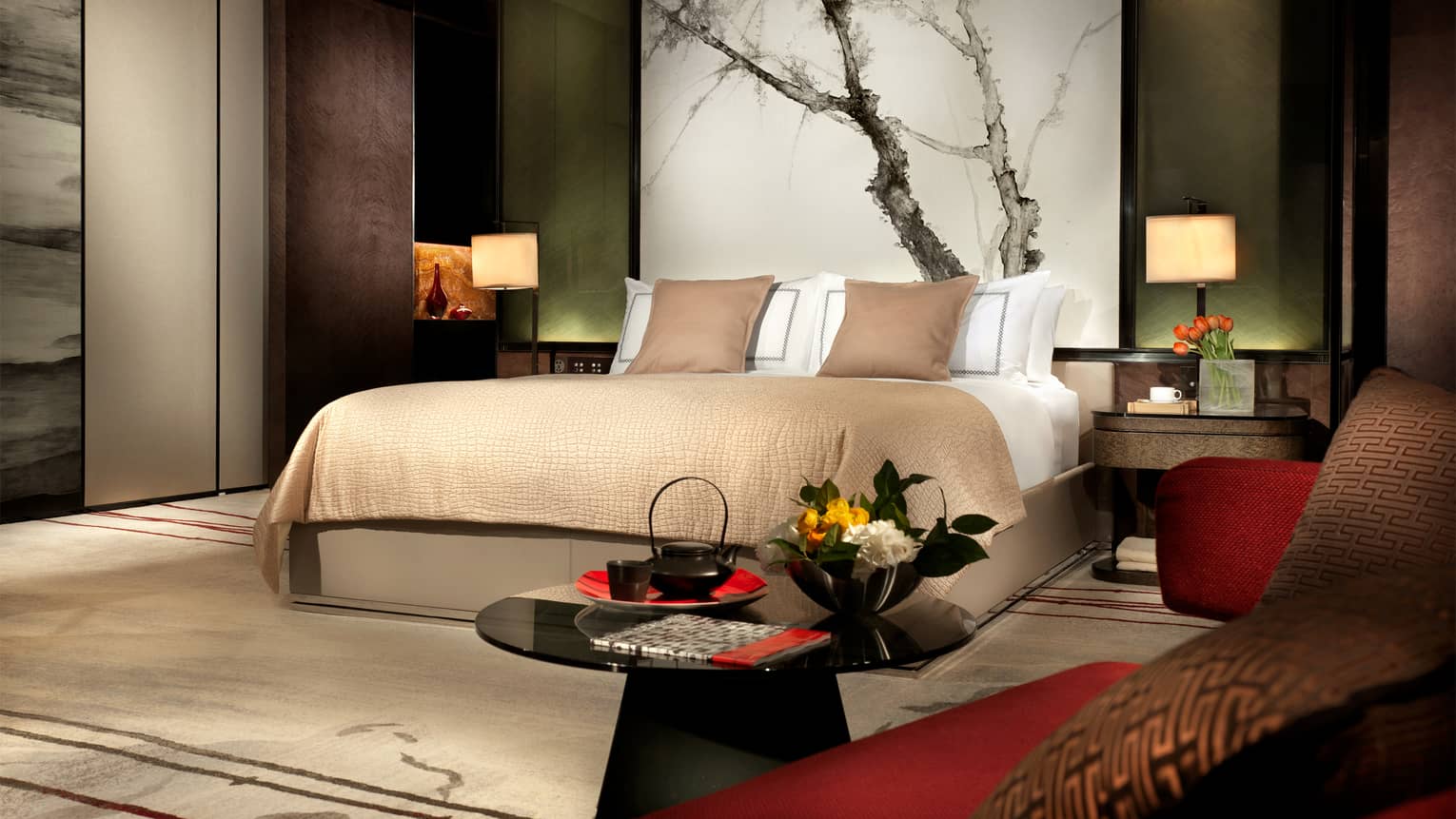 Hotel room platform bed with headboard painting of tree branches, deep brown, red and green decor