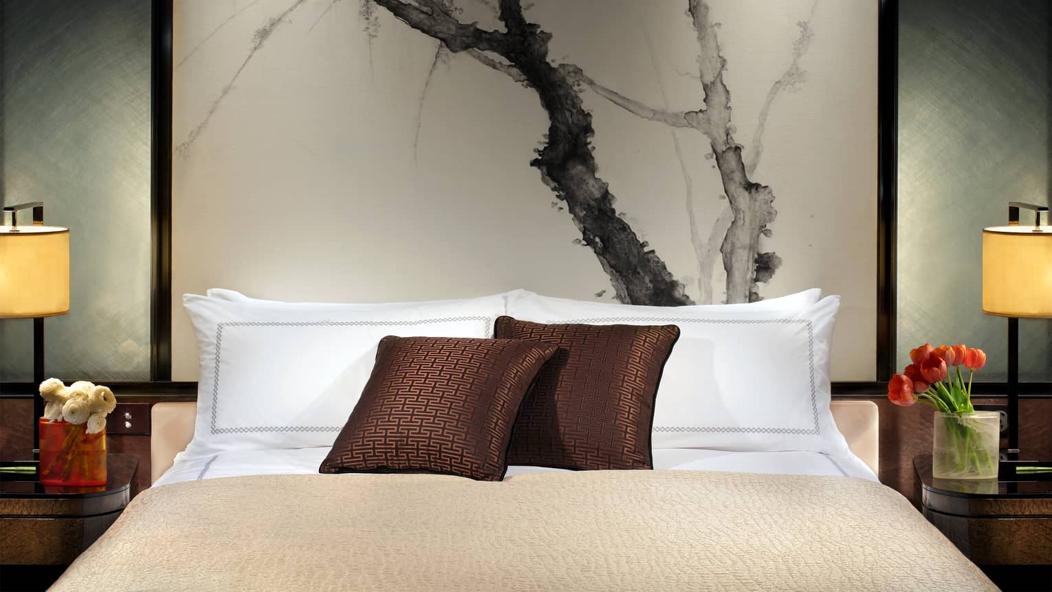 Close-up of bed with chocolate-brown accent pillows, tall headboard with black-and-white painting of branches
