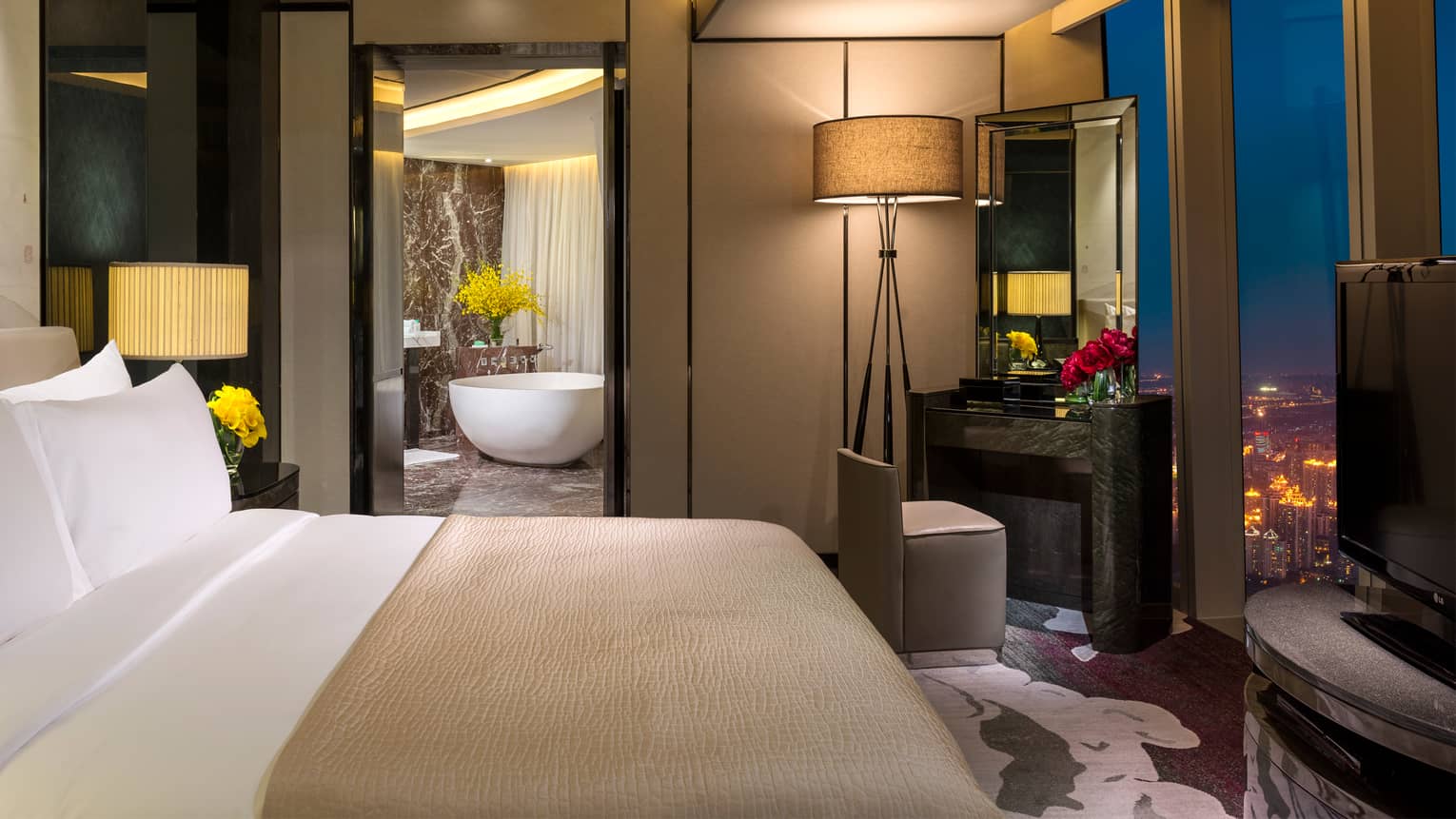 Deluxe Suite at night with king-size bed, vanity and mirror, open door to bathroom with free-standing white tub
