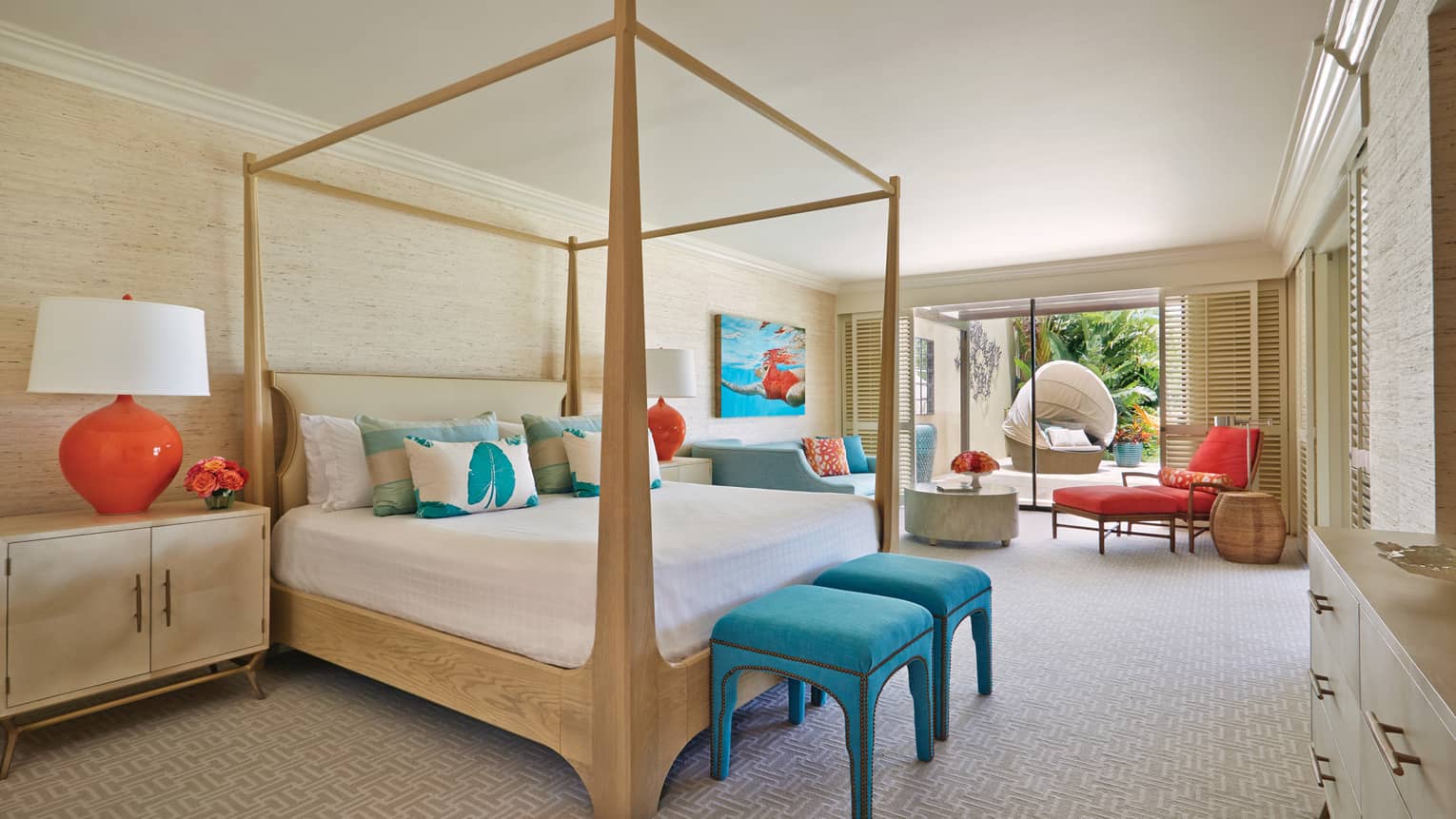 Spacious bedroom with a light wood four-poster bed, turquoise and orange accents and seating area, leading to a patio with garden view