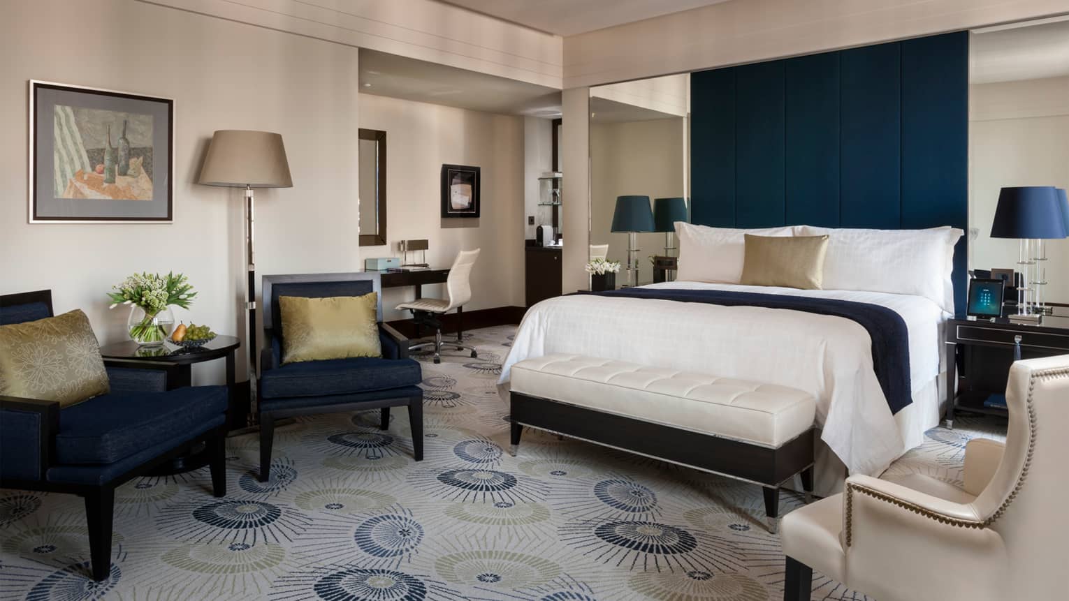 Premier room dark blue armchairs with gold pillows, bed with dark blue fabric headboard, light area rug