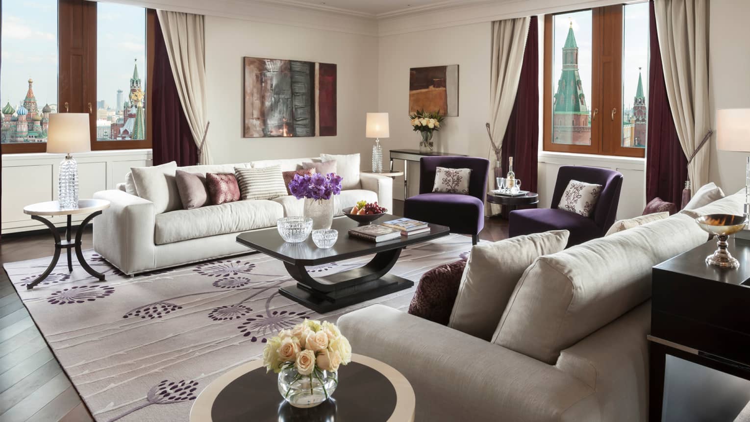Living room in hotel suite with white sofas, purple pillows and accents, floral area rug