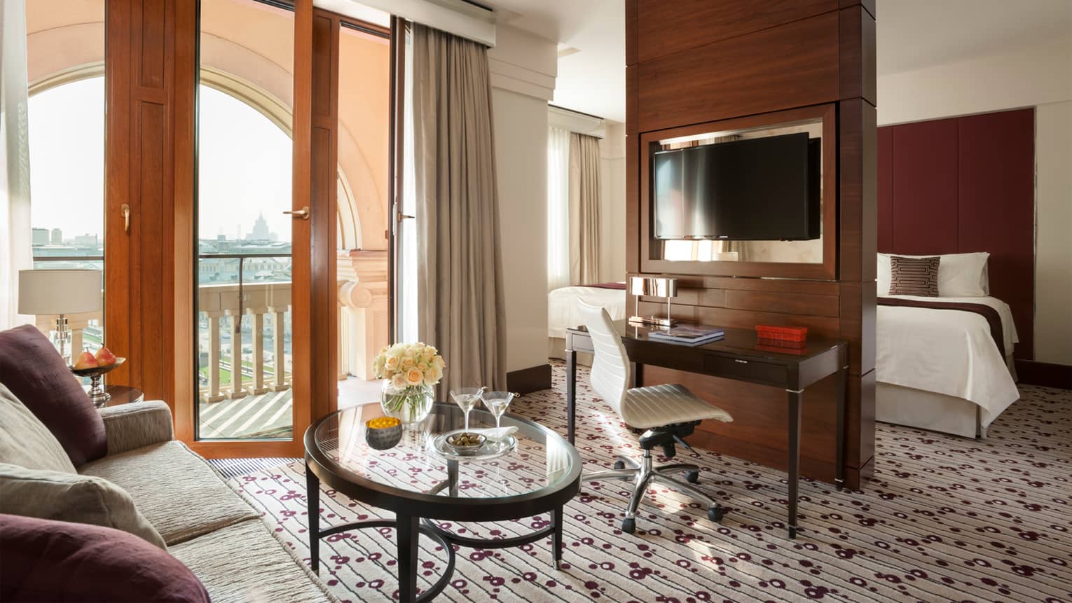 Living space with desk, TV and wood room divider leading to bedroom, wood-and-glass door open to balcony