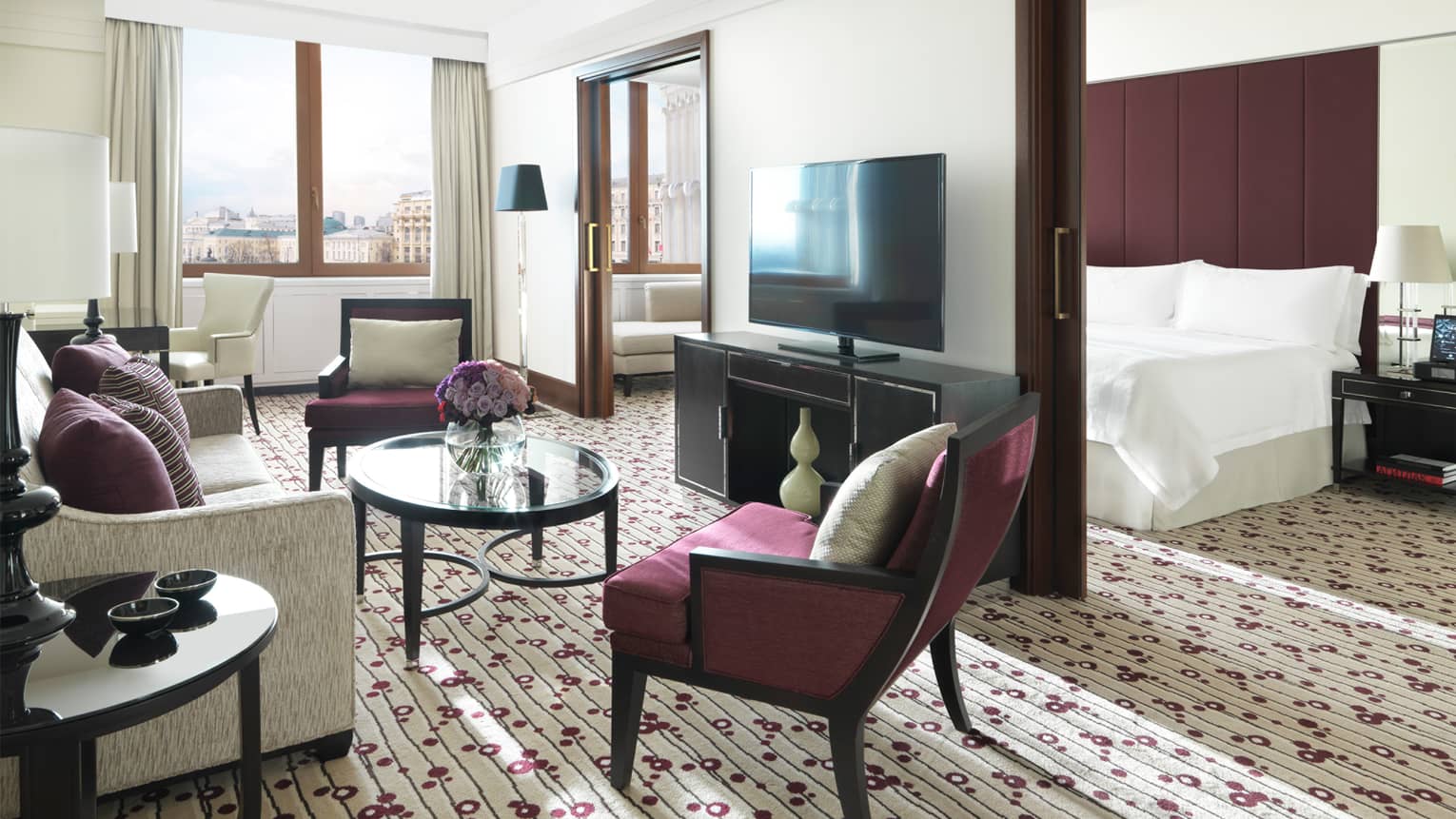 Executive Suite living area with burgundy accent chairs, flowers in glass vase, flat-screen TV on wall concealing bed