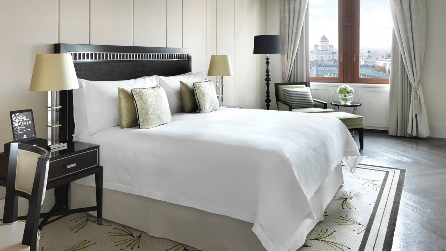 Sunny Deluxe Suite bedroom with gold accent pillows, ivory wall panel, nightstand with laptop computer