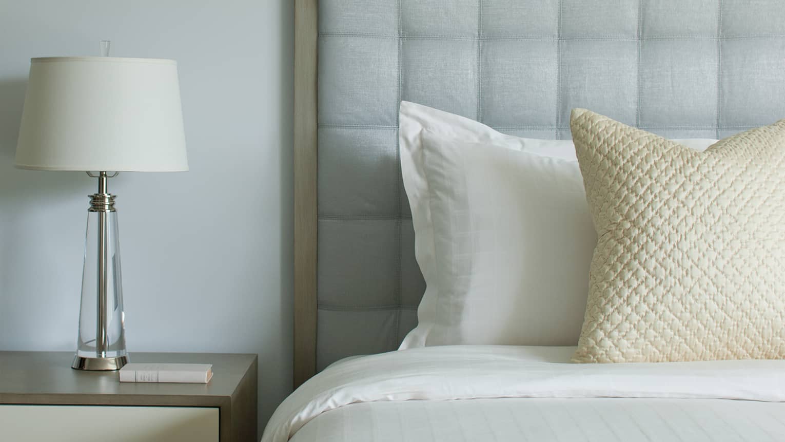 Close-up of Accessible Ocean-View Room with white bed, ivory accent pillow, grey padded headboard, lamp