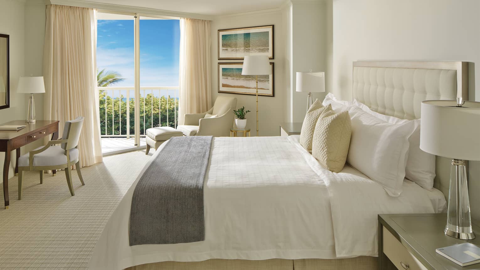 Resort-View Room bed with grey bedspread, white armchair, desk and balcony overlooking palm trees
